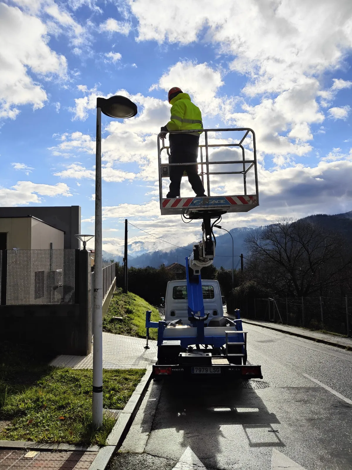 Técnico en la cesta de la plataforma elevadora junto a una farola renovada